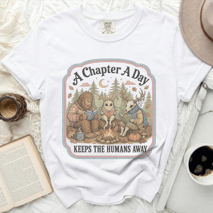 Bigfoot, moth, and deer read books by a campfire, "A Chapter A Day Keeps The Humans Away."
