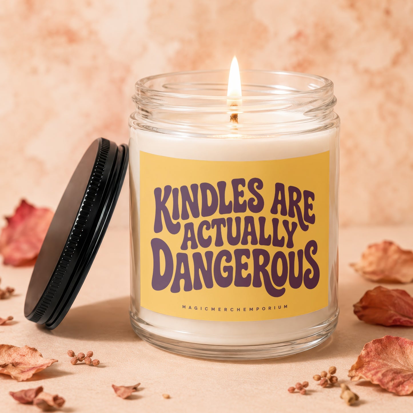 Glass candle with lit wick and yellow label reading "KINDLES ARE ACTUALLY DANGEROUS".