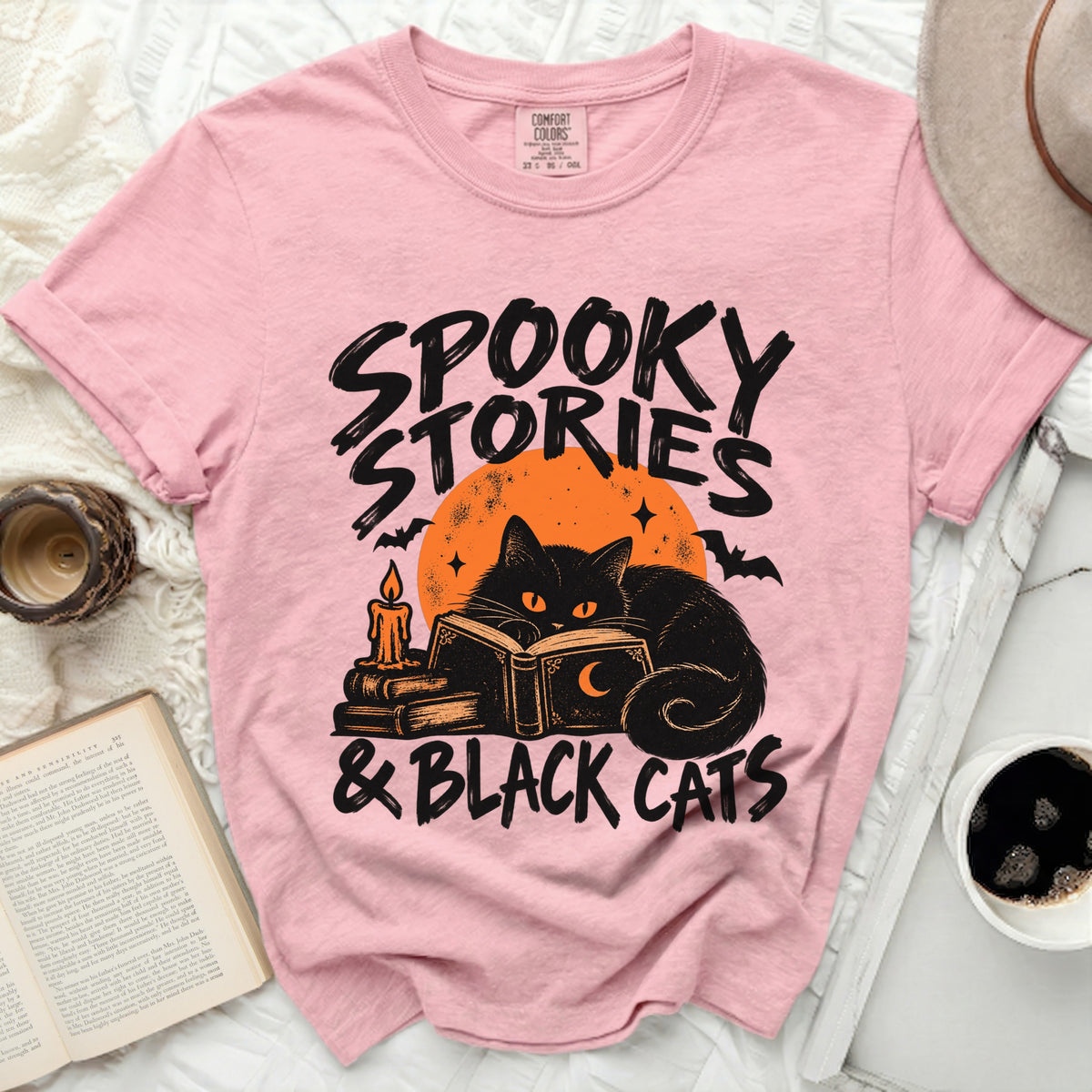 Pink t-shirt with graphic of black cat reading spooky stories and black cats.