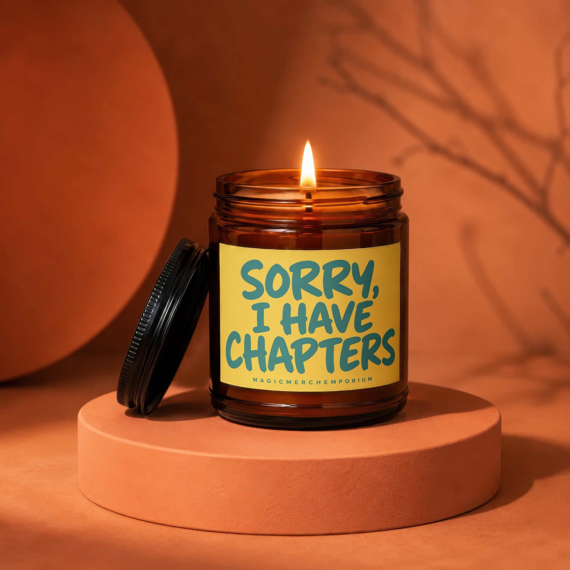 Amber jar candle with a lit flame and a label that says "Sorry, I Have Chapters".