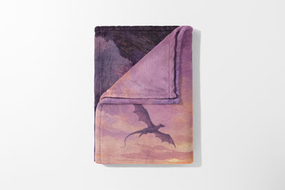 Fuzzy blanket with dragon flying through a sunset sky on purple and pink background.