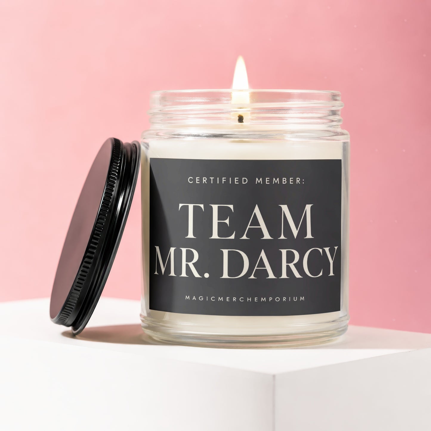 Glass candle with lit wick, black lid, and label reading "Certified Member: Team Mr. Darcy".