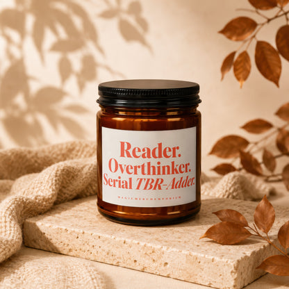 Amber candle with black lid, white label reads "Reader. Overthinker. Serial TBR-Adder."