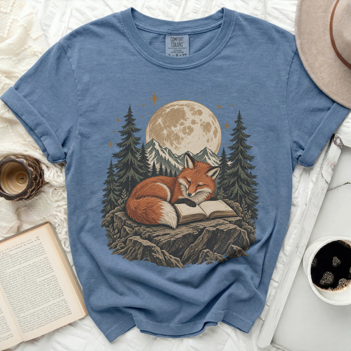 Blue t-shirt with a graphic of a fox reading a book under a moonlit sky.