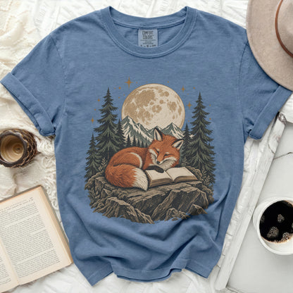 Blue t-shirt with a graphic of a fox reading a book under a moonlit sky.