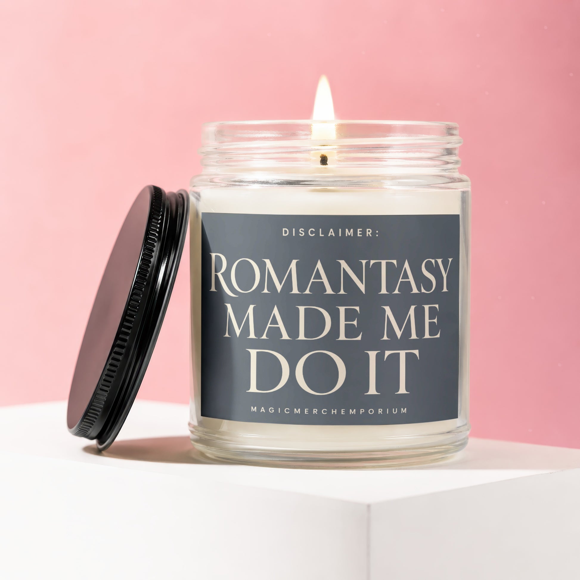 Lit glass candle with a black lid and label that reads "ROMANTASY MADE ME DO IT".