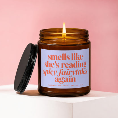 Amber jar candle with lit flame, text reads "smells like she's reading spicy fairytales again".