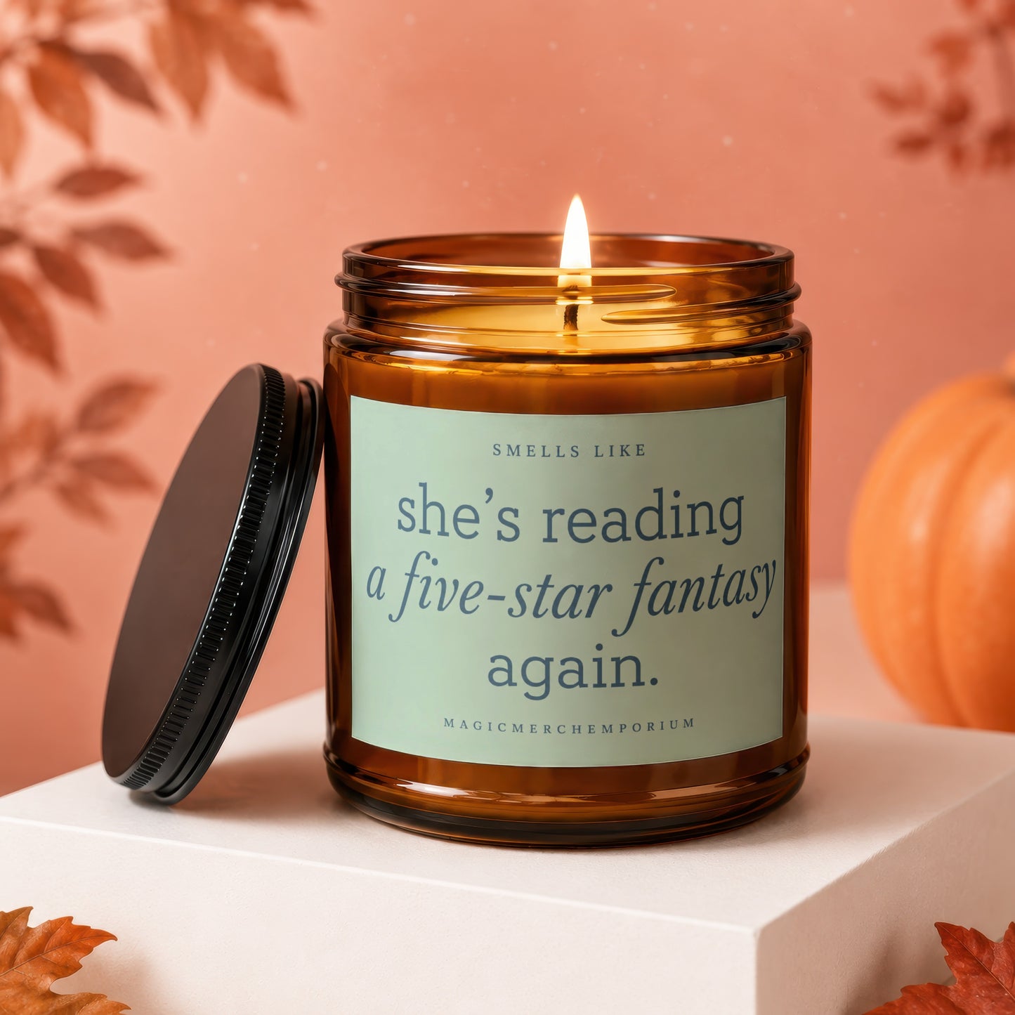Amber candle with "she's reading a five-star fantasy again" text, lid removed, pumpkin and leaves background.