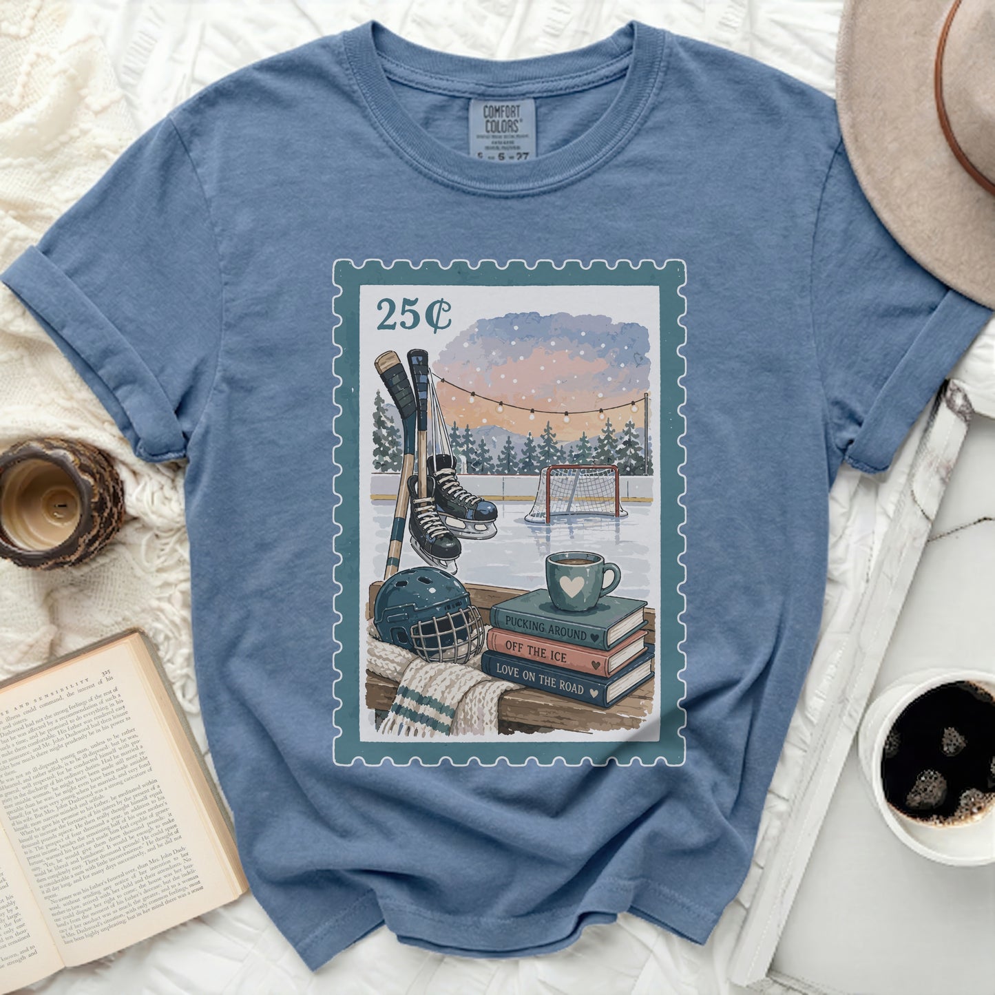 Blue t-shirt with a postage stamp graphic of hockey gear and books.