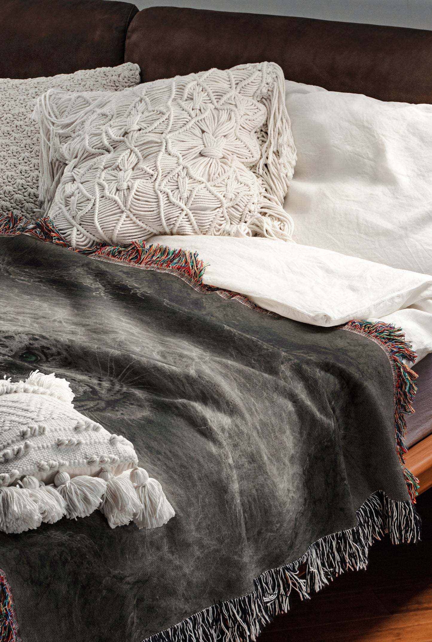 a cozy and inviting bedroom scene, featuring a bed with a gray blanket and white pillows, a brown leather couch, and a wooden floor.