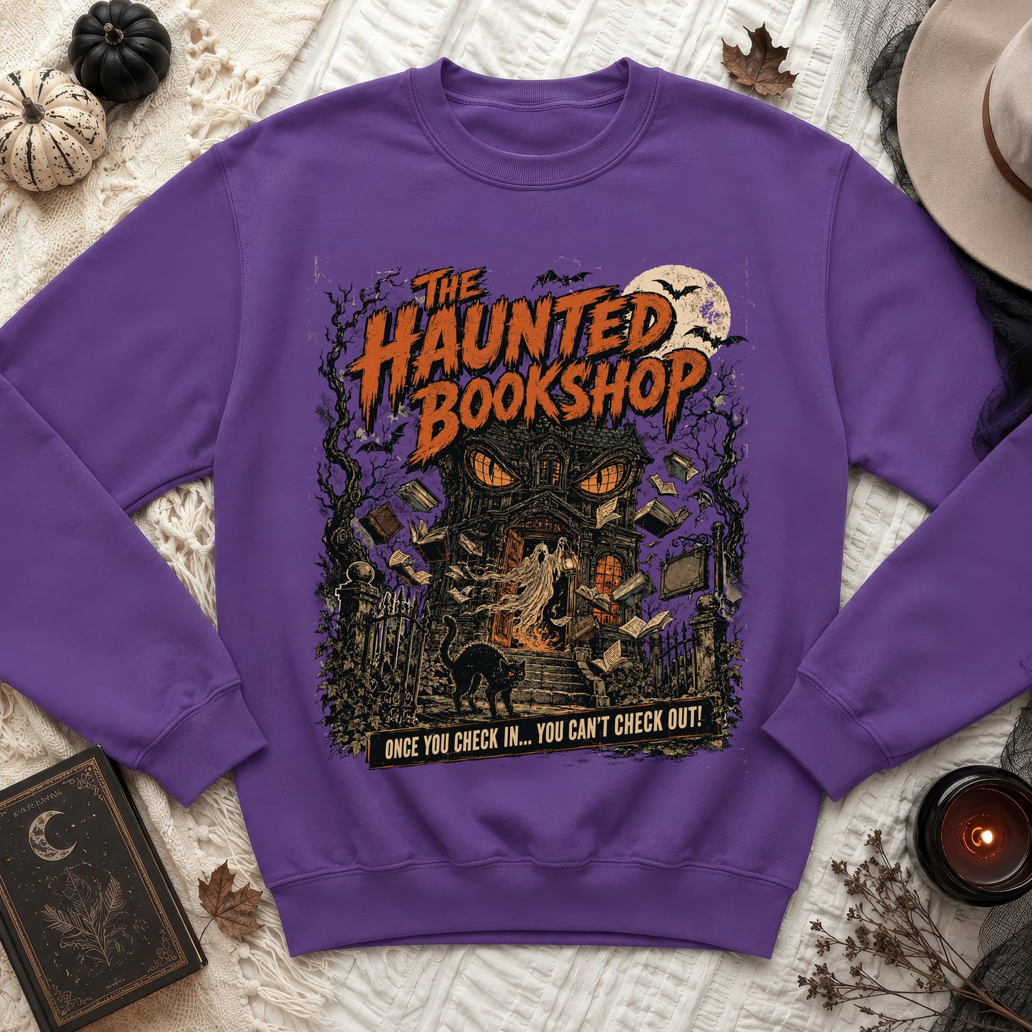 Purple sweatshirt with "The Haunted Bookshop" graphic featuring a haunted house, ghost, and cat.