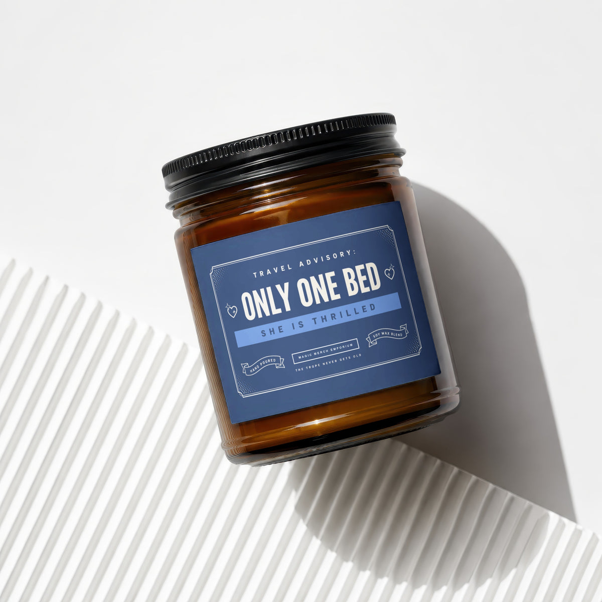 Amber glass candle with a blue label reading "TRAVEL ADVISORY: ONLY ONE BED"