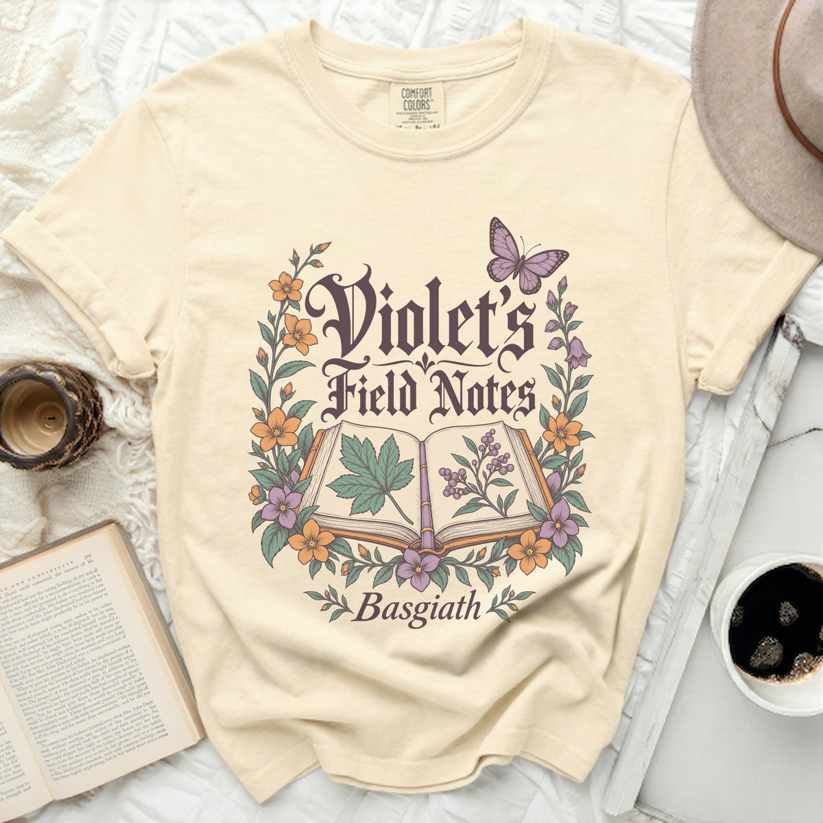 Cream t-shirt with "Violet's Field Notes Basgiath" in gothic font surrounded by flowers and a butterfly.