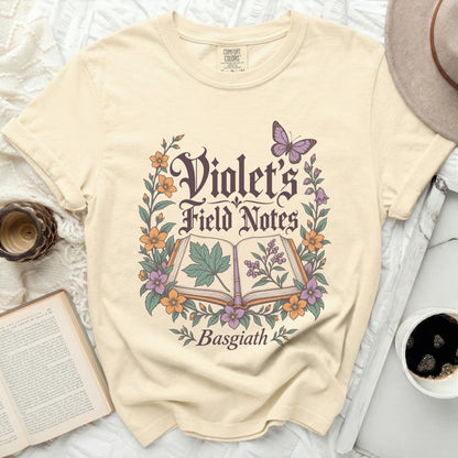 Cream t-shirt with "Violet's Field Notes Basgiath" in gothic font surrounded by flowers and a butterfly.