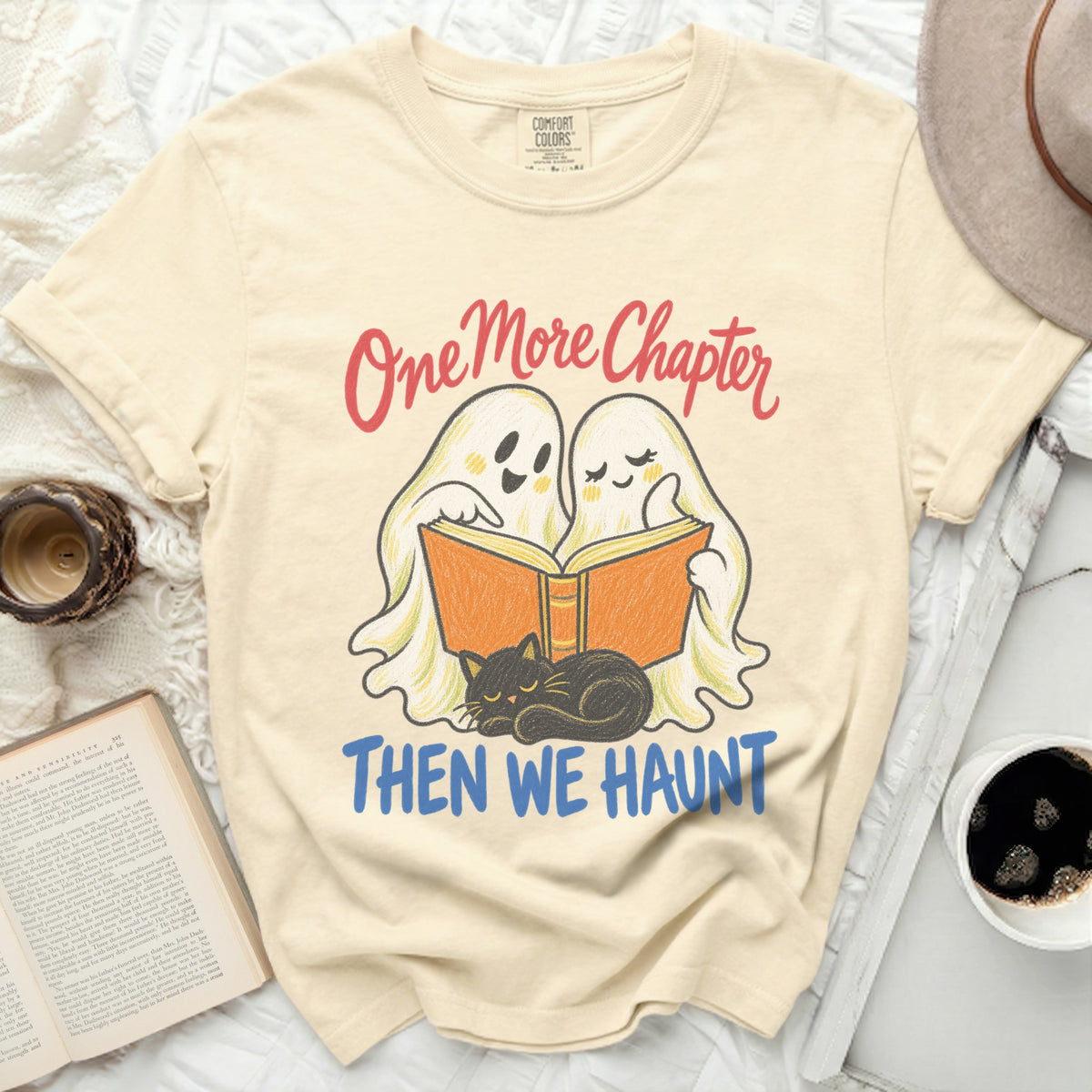 Cream t-shirt with ghosts reading and cat, saying "One More Chapter Then We Haunt".