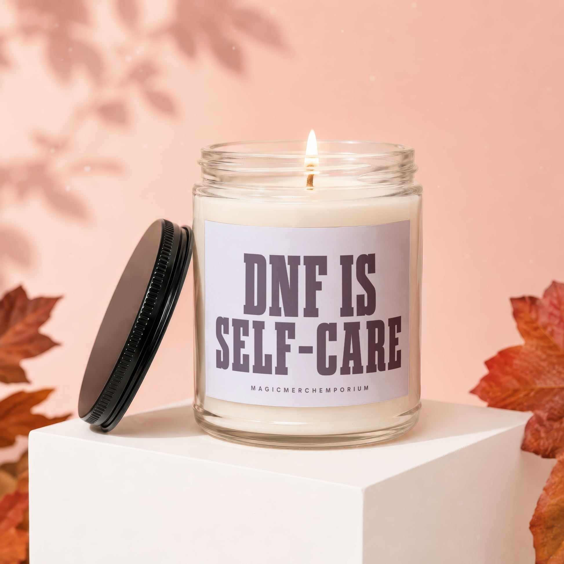 Glass candle with lid off, "DNF IS SELF-CARE" text, next to fall leaves.