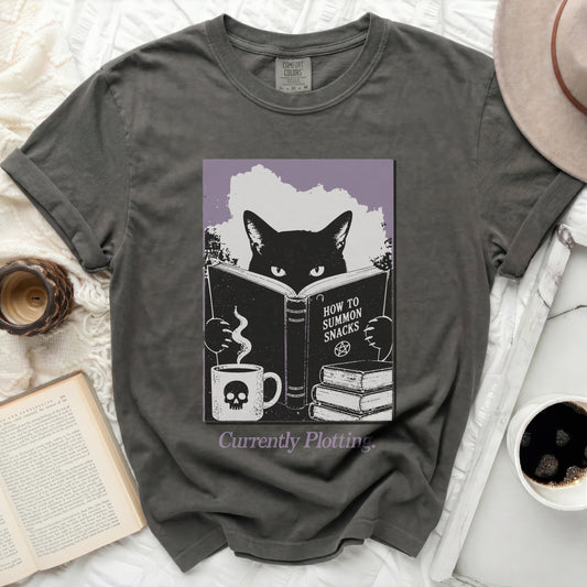 Black cat reading "How to Summon Snacks" with skull mug and books.