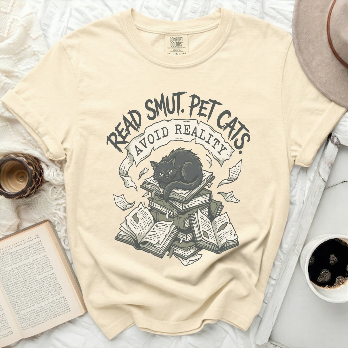 Cream t-shirt with "READ SMUT. PET CATS AVOID REALITY" and a black cat on books.