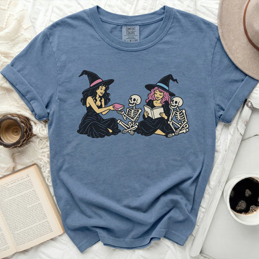 Witches reading to skeletons on a blue t-shirt.