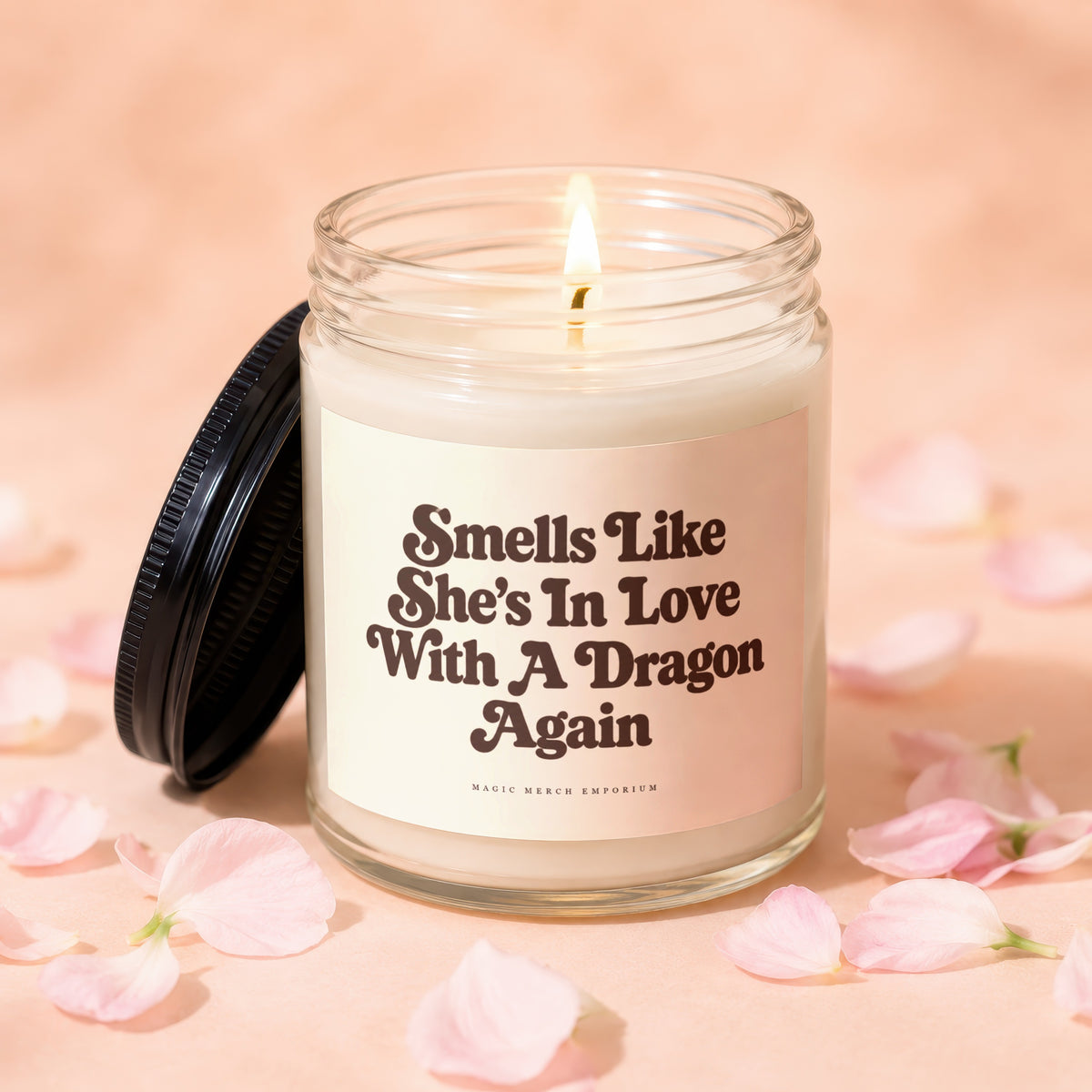 Lit candle with text "Smells Like She's In Love With A Dragon Again" and "MAGIC MERCH EMPORIUM."