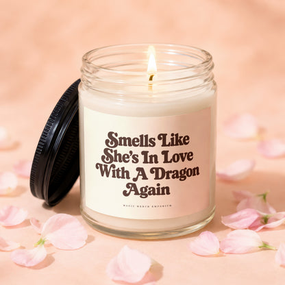 Lit candle with text "Smells Like She's In Love With A Dragon Again" and "MAGIC MERCH EMPORIUM."