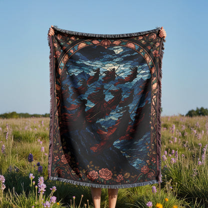 A person is holding up a large, colorful blanket with a detailed design, standing in a field of purple flowers.