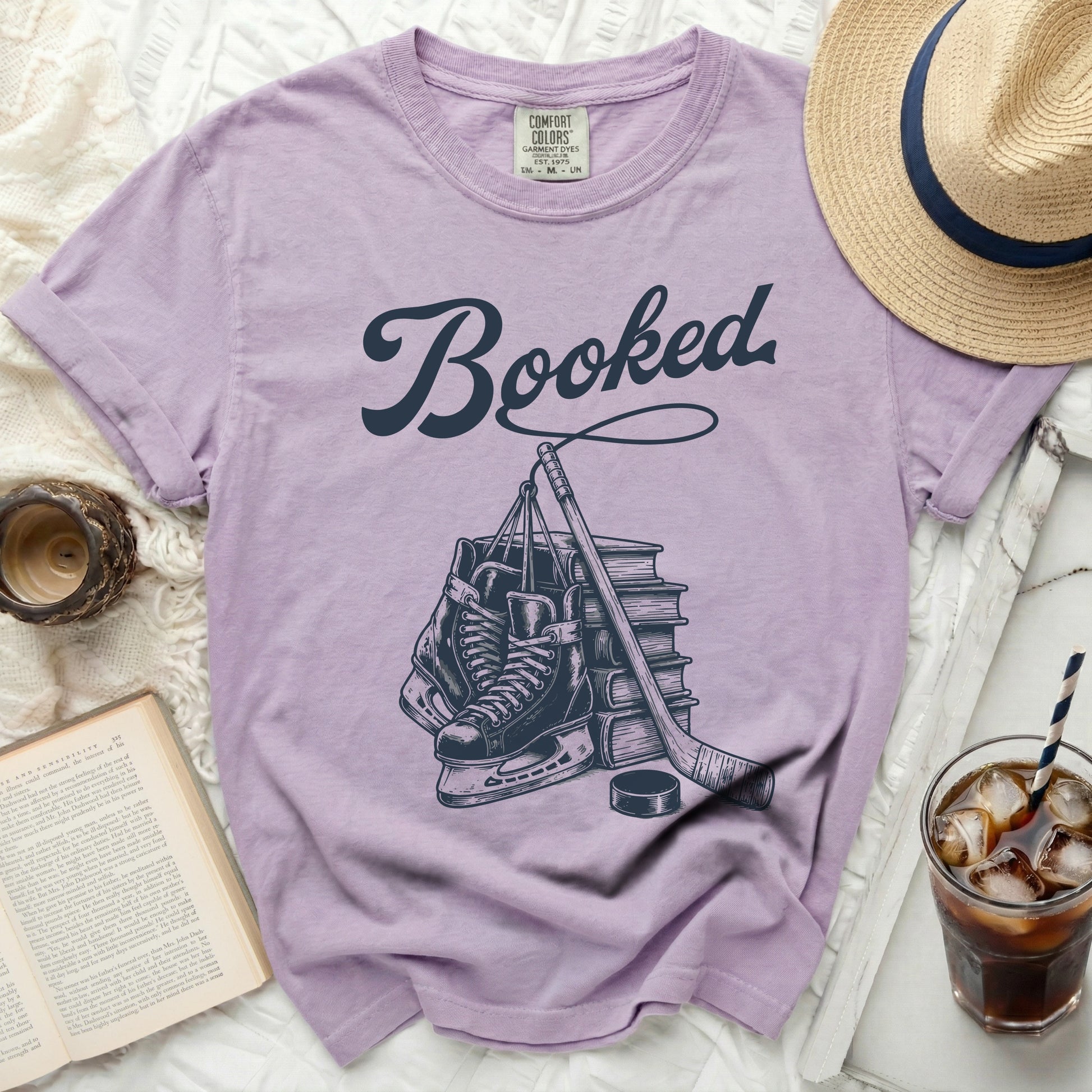 Lavender t-shirt with "Booked" text and hockey equipment illustration.