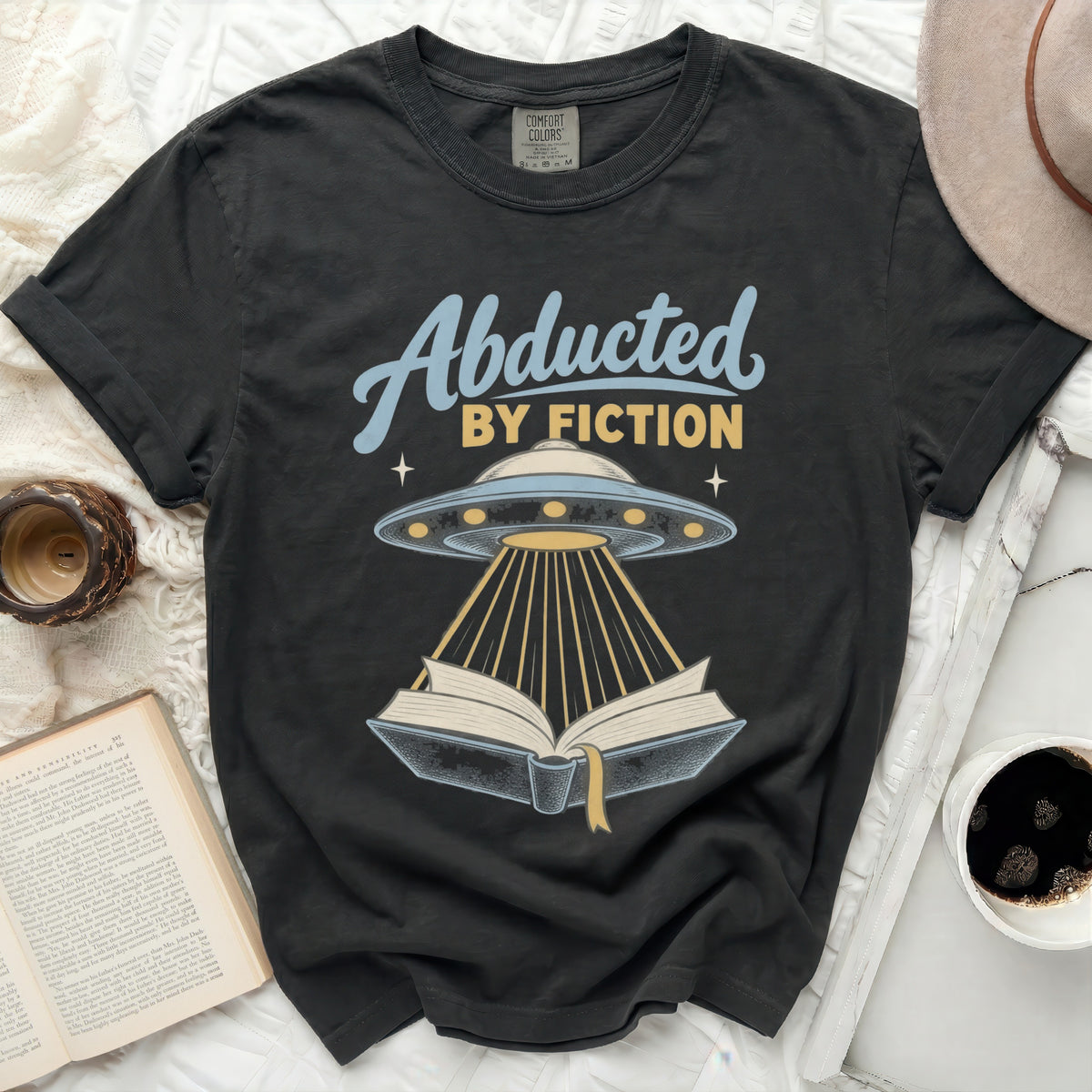 Black t-shirt with "Abducted by Fiction" text, UFO, and open book graphic.