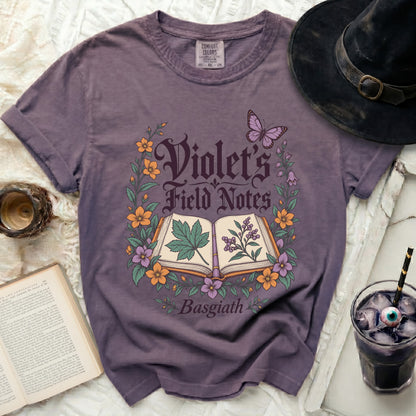 Purple t-shirt with "Violet's Field Notes Basgiath" text and botanical illustration.