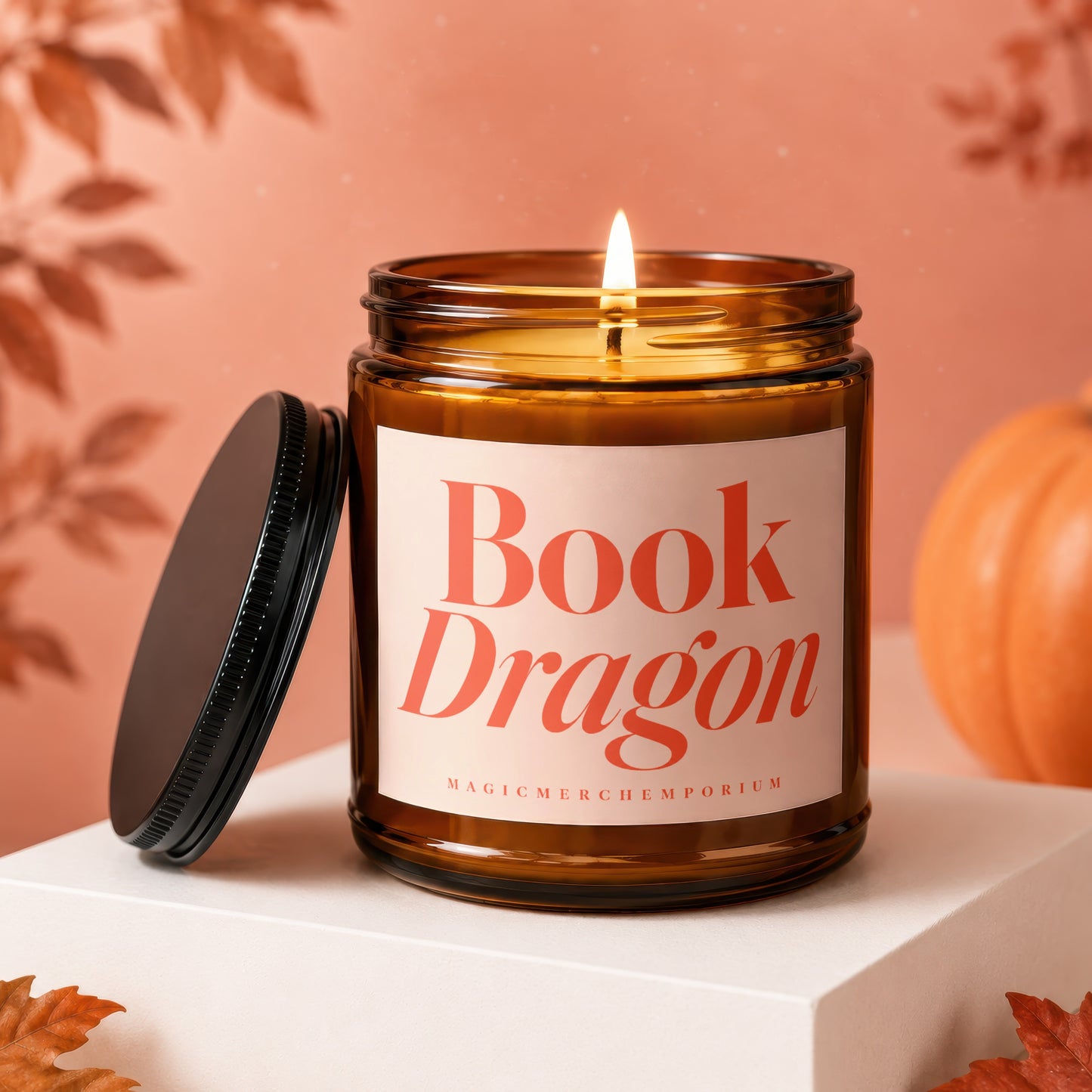 Amber jar candle with lit wick labeled "Book Dragon" on a white pedestal.
