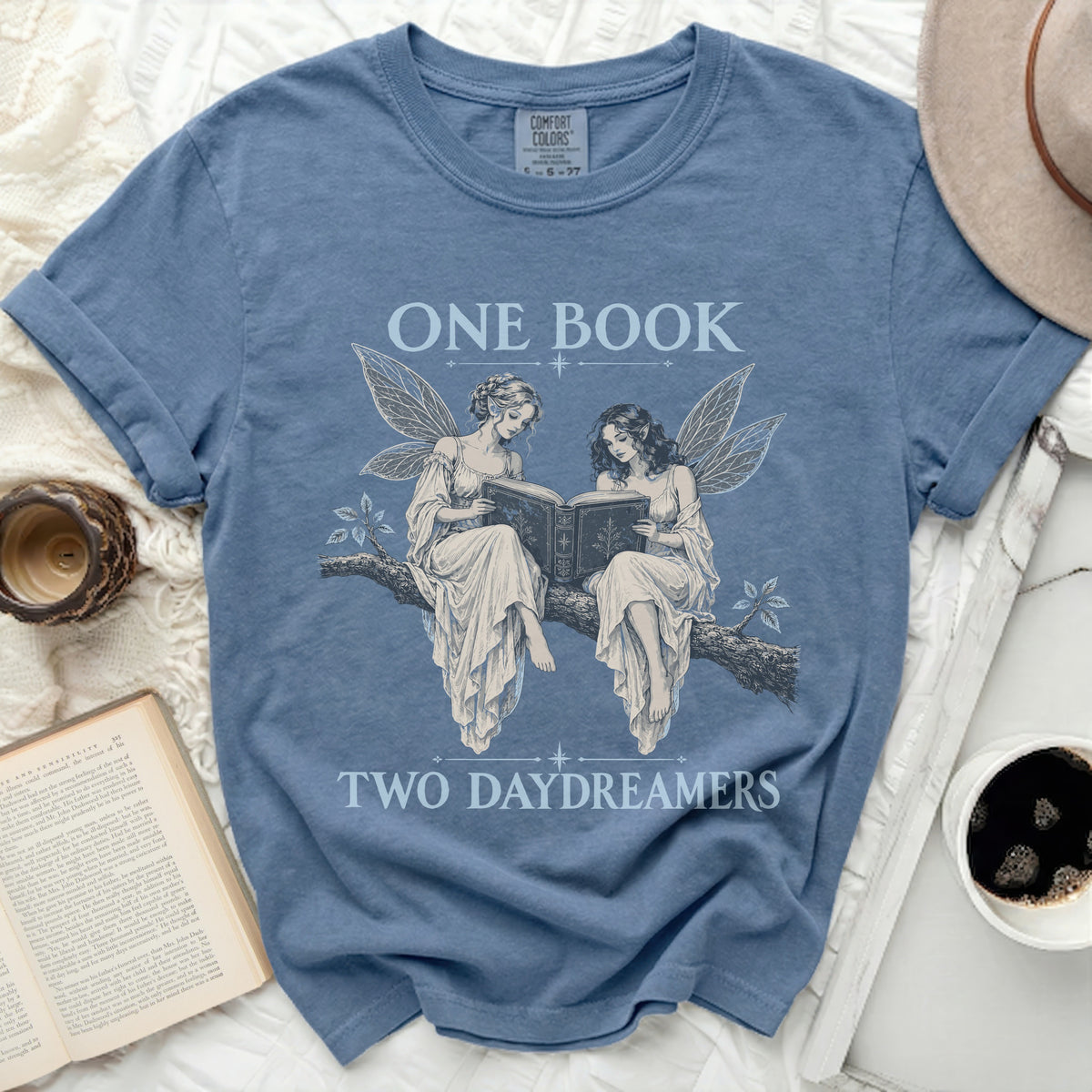 Blue t-shirt with fairies reading a book, text "ONE BOOK TWO DAYDREAMERS".