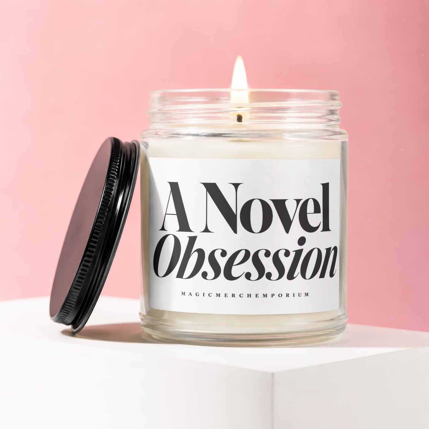 Glass jar candle with lit wick, black lid, and label reading "A Novel Obsession".
