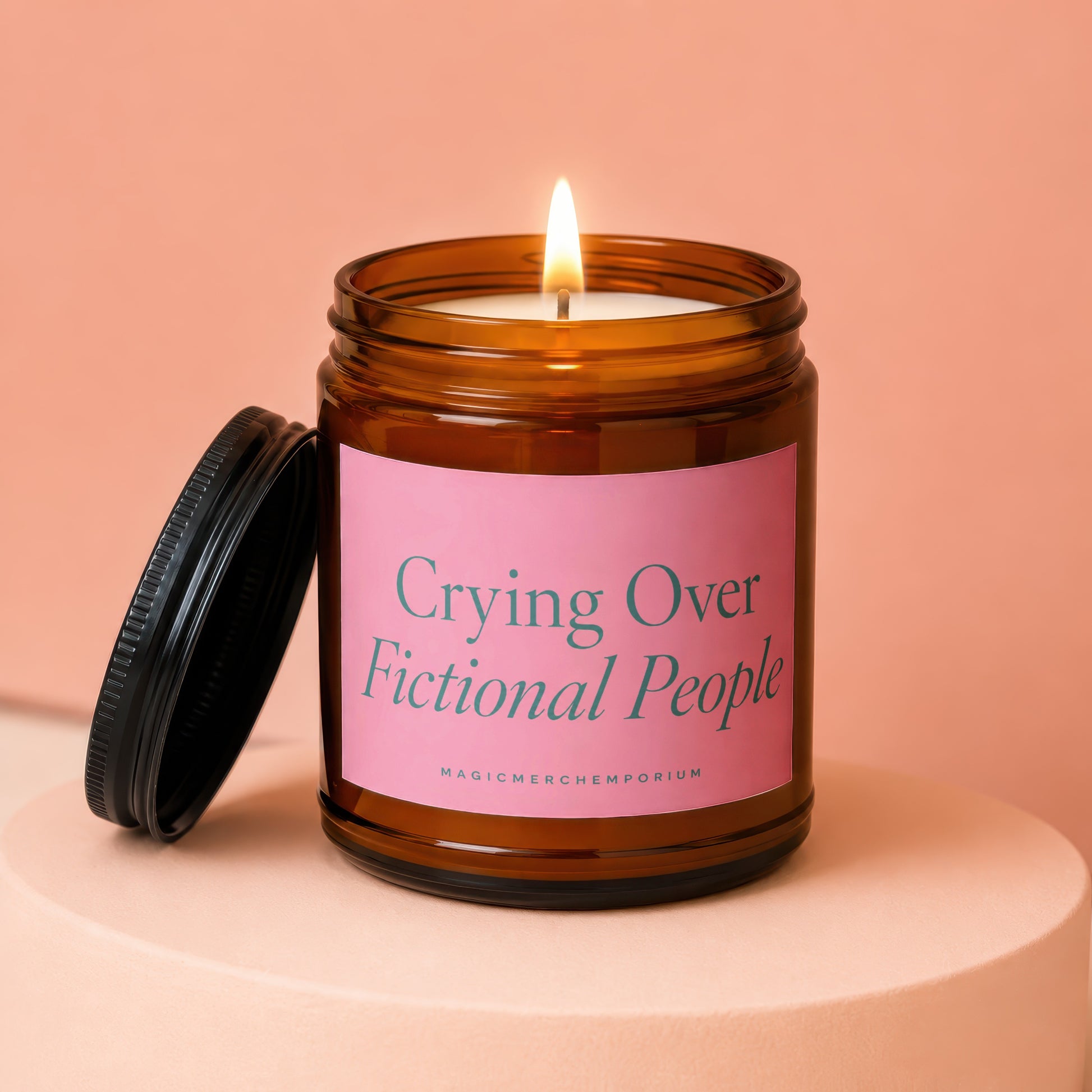 Amber jar candle with lit wick and lid removed, reading "Crying Over Fictional People".