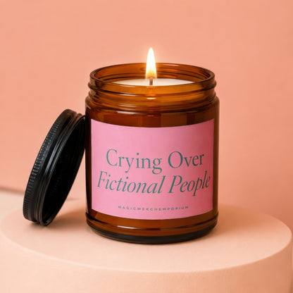 Amber jar candle with lit wick and lid removed, reading "Crying Over Fictional People".