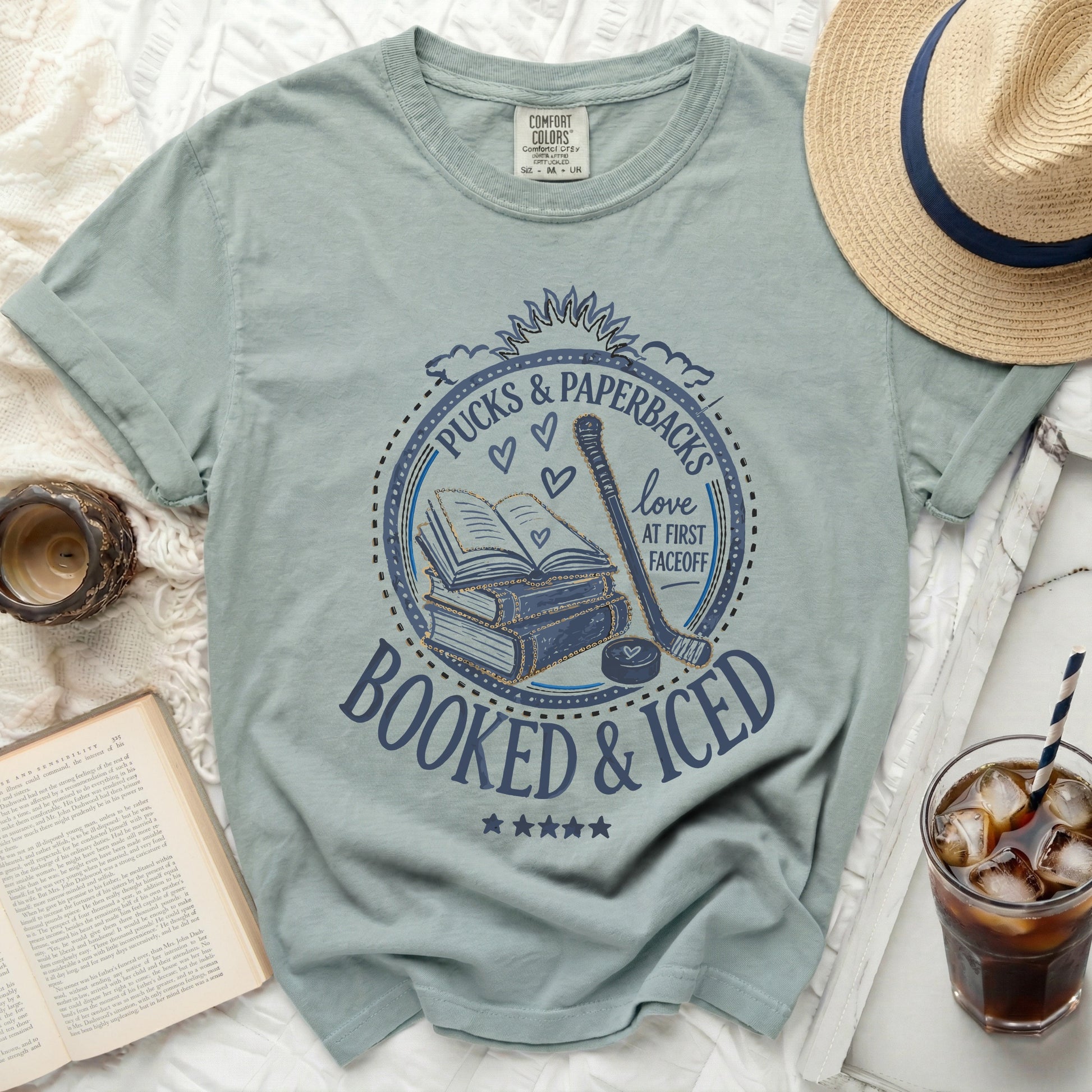 Blue graphic tee with "Booked & Iced" text, books, hockey puck, and stick.
