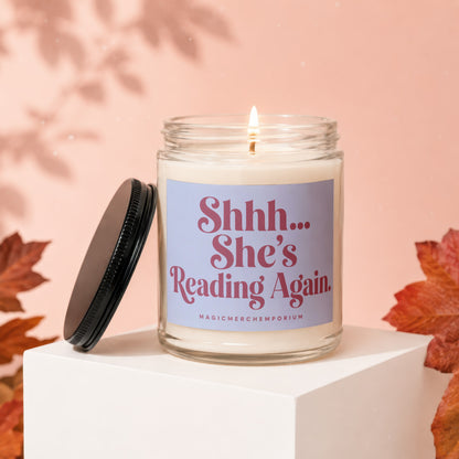 Glass candle with lit wick and lid removed, reads "Shhh... She's Reading Again."