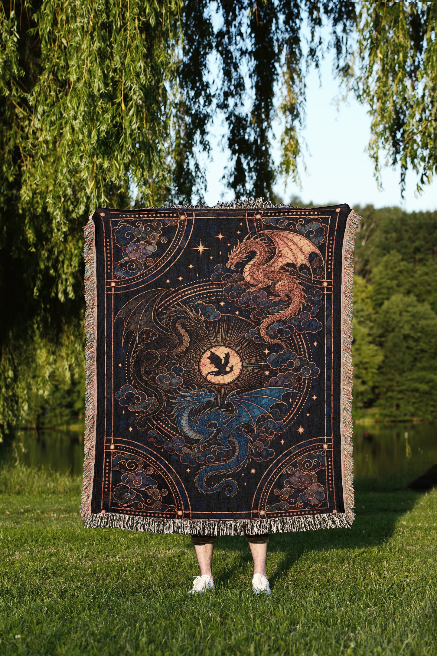A person stands in a grassy field, holding a large, intricately designed blanket featuring a dragon and a starry night sky.
