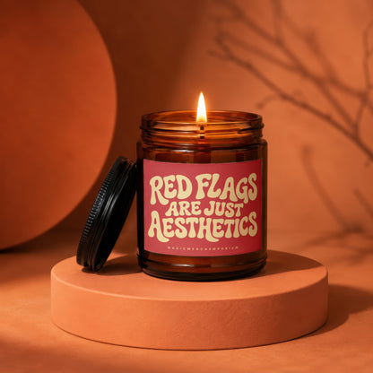Amber jar candle with lit wick, reading "Red Flags Are Just Aesthetics".