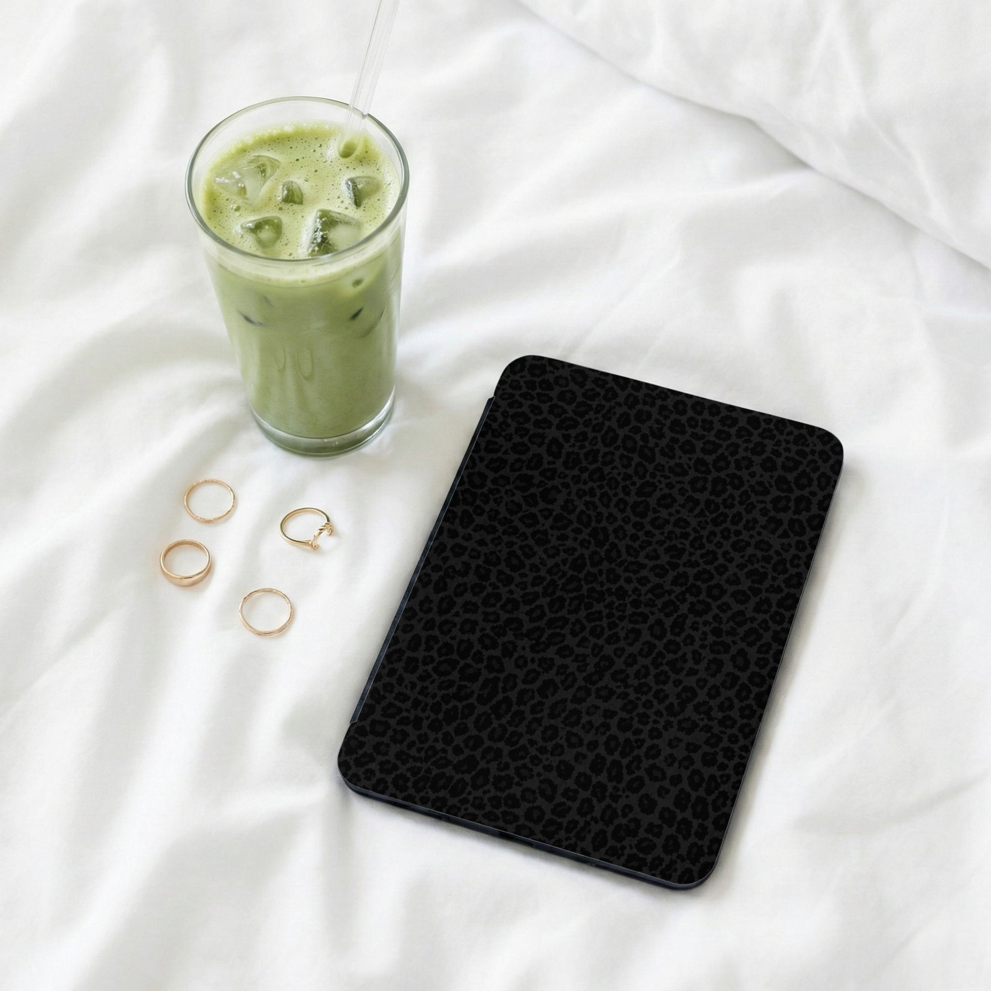 Black leopard print tablet case next to a glass of iced matcha and gold rings.