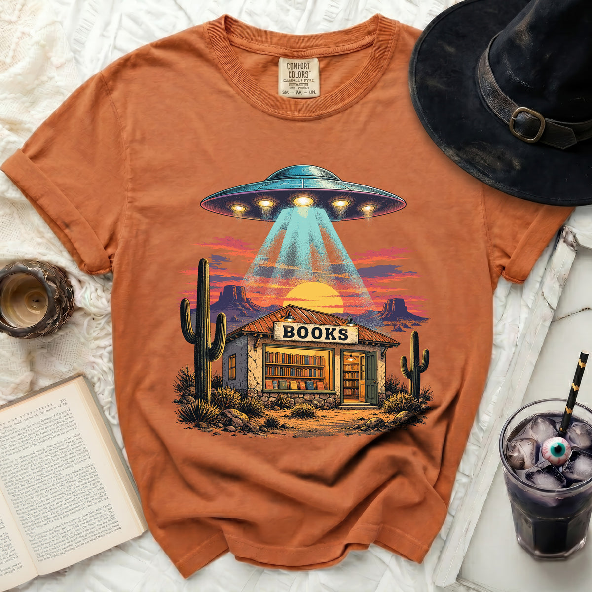 Orange t-shirt with a graphic of a UFO beaming into a desert bookstore.