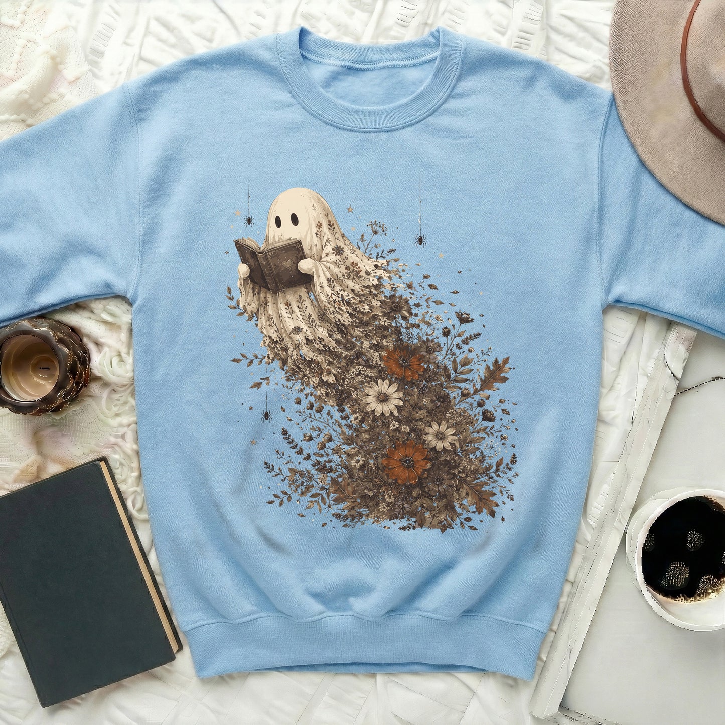 Light blue sweatshirt with a ghost reading a book amidst autumn leaves and flowers.