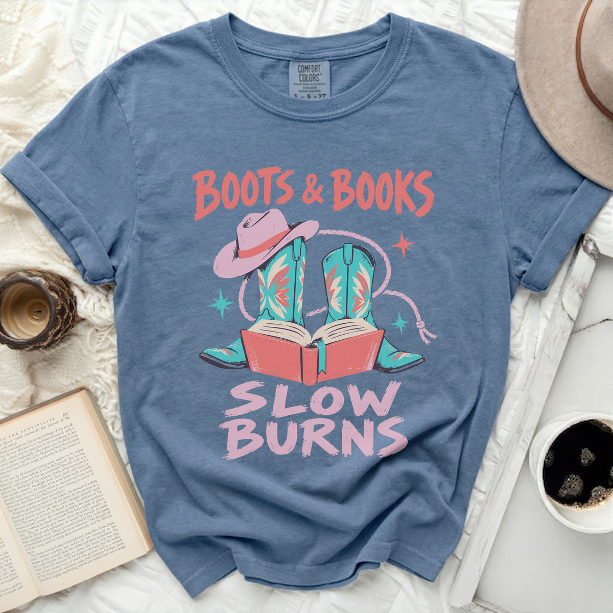 Blue t-shirt with "Boots & Books Slow Burns" graphic featuring boots, a hat, and books.