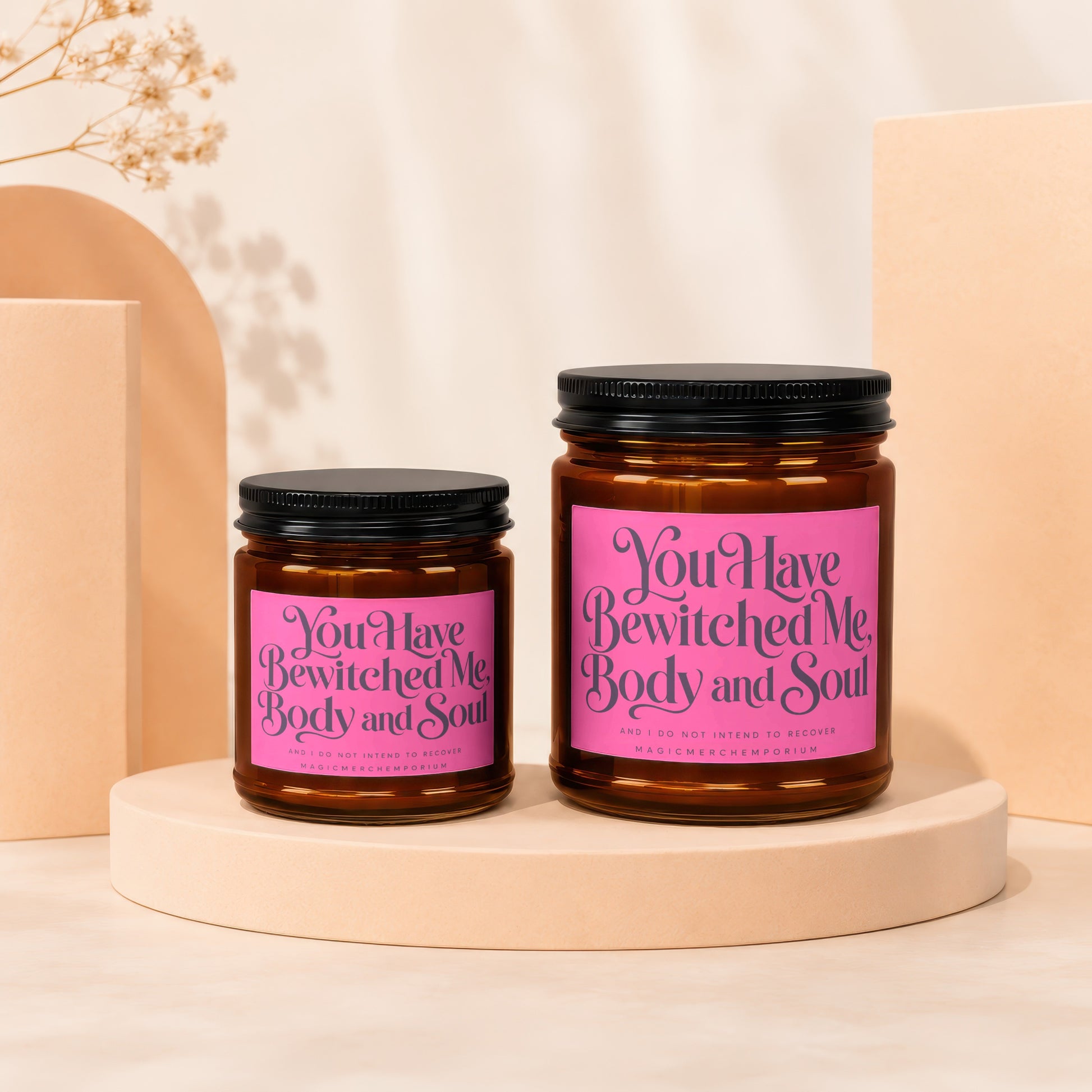 Two amber glass candles with pink labels that say "You Have Bewitched Me, Body and Soul."