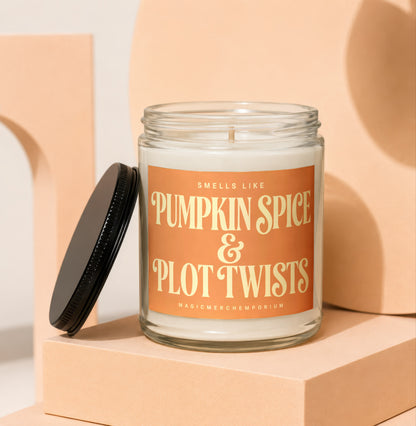 Glass jar candle with orange label reading "Smells Like Pumpkin Spice & Plot Twists".