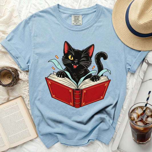 Black cat peeking out of a red book with text on a light blue t-shirt.