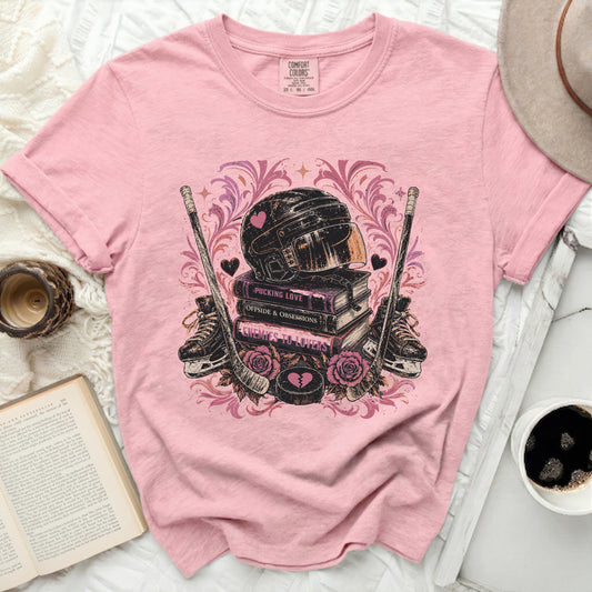 Pink t-shirt with hockey helmet, skates, crossed sticks, and books.