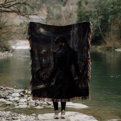 A person stands on a rock, holding a large, dark-colored blanket with a painting of a cityscape on it, facing a body of water.