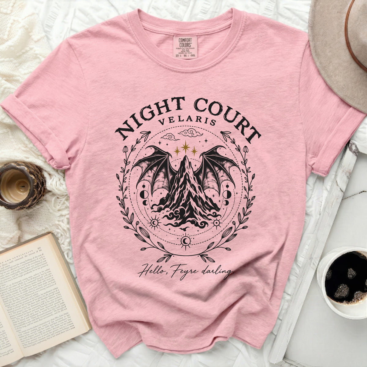 Pink t-shirt featuring a black graphic of winged mountains with celestial motifs, the text Night Court Velaris, and Hello Feyre darling.