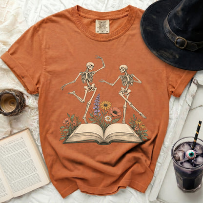 Orange t-shirt with two dancing skeletons on an open book with flowers.