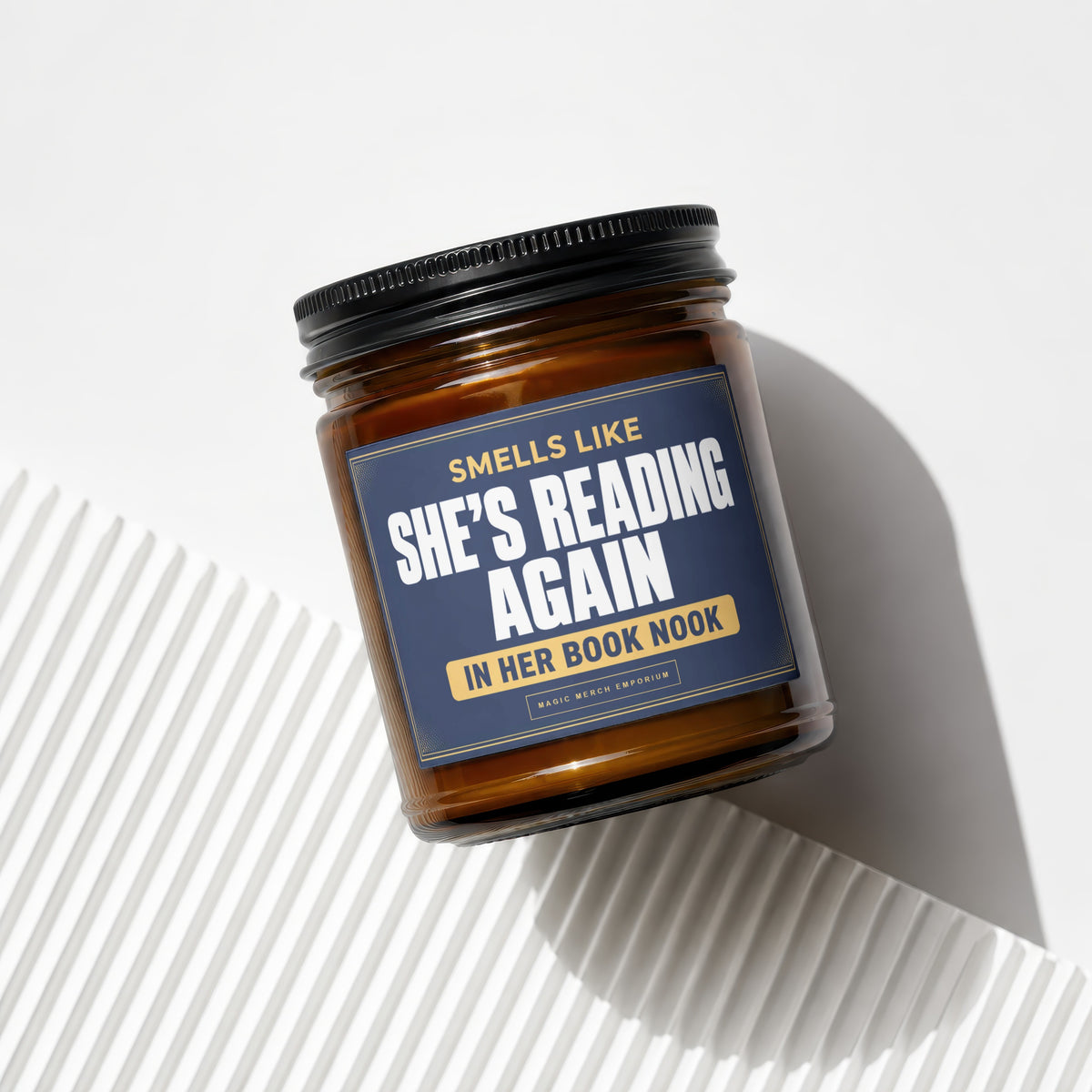Amber glass candle with dark blue label reading "Smells Like She's Reading Again In Her Book Nook".